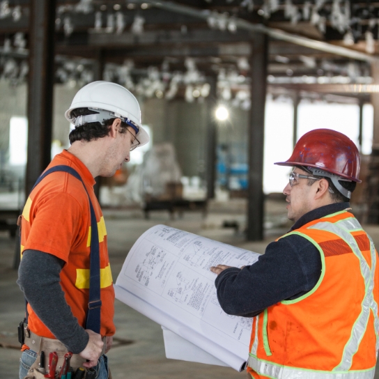 Two workers in high visibility jackets looking at a plan.